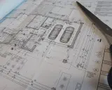 Projekt architektoniczno budowlany domu z garażem na dwa samochody. Nożyczki leżą na planie.