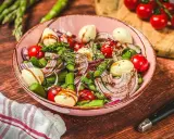 Frischer Spargelsalat mit Ei, Tomaten, roten Zwiebeln und Mozzarella-Kugeln, beträufelt mit Balsamico-Dressing.
