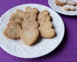 Stos ciasteczek cytrynowych w kształcie serc, posypanych cukrem pudrem, na białym talerzu.