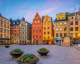 Färgglada hus på ett kullerstens torg i Gamla Stan, Stockholm, med blomkrukor i förgrunden.