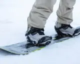 Snowboarder w beżowych spodniach zapina wiązania snowboardowe szybkie zapinanie. Gotowy na jazdę po śniegu.
