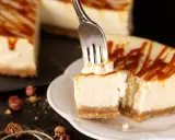 Une fourchette prélève un morceau crémeux de cheesecake, révélant le fromage frais onctueux sous un filet de caramel.