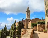 Un borgo nei comuni Val d'Orcia: un campanile svetta tra cipressi e case antiche, con un bar all'aperto.