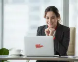 Uśmiechnięta kobieta przy laptopie z logo "New Heroes Academy" odkrywa, jak się przebranżowić.