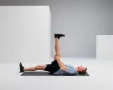 Mann liegt auf Matte, dehnt Bein für Hamstring Training.