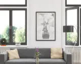 Sofá gris con cojines, cuadro de un ángel con alas, como un cristal guardian sun, y ventanas con vistas a árboles.