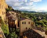 Panoramica di borghi toscana in treno, con case in pietra e tegole rosse su colline verdi sotto un cielo nuvoloso.