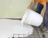 En person häller ut ett vitt material ur en stor hink över ett armeringsnät. Inspiration för betonggolv.