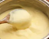 Une cuillère en bois remue une crème pâtissière maison onctueuse dans une casserole.