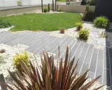Chemin en dalles grises et gravier blanc, pelouse verte et plantes décoratives. Un jardin facile d'entretien.