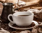 Eine Tasse heißer Espresso Mokka, umgeben von gerösteten Kaffeebohnen und einer traditionellen Mokkakanne.