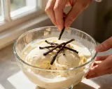 Des mains ajoutent des gousses de vanille sur un parfait glacé à la vanille dans un bol en verre.