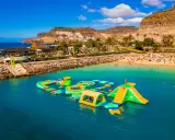 Divertimento acquatico a Gran Canaria con bambini: scivoli gonfiabili e giochi in mare su una spiaggia affollata.