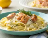 Tagliatelle al salmone: breite Bandnudeln in cremiger Sauce mit saftigen Lachsstücken und frischen Kräutern, garniert mit Dill.