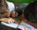Due bambini studiano insieme, uno scrive mentre l'altro indica il libro. Un esempio di peer learning.