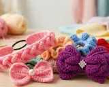 Coletero crochet de varios colores, con lazos y flores, junto a ovillos de lana y ganchillos.