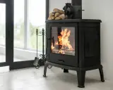 Estufa de leña con fuego encendido, lista para instalarse con salida horizontal. Leña apilada y herramientas de chimenea.