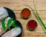 Rouleaux de printemps frais sur une assiette noire, accompagnés de deux sauces : une sauce aigre douce orangée et une sauce rouge.
