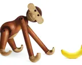 En träapa från Kay Bojesen tittar nyfiket på en banan. Olika kay bojesen apa storlekar finns tillgängliga.