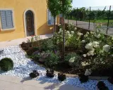 Ingresso esterno di una villetta con ghiaia bianca, piante fiorite e un vialetto. Belle idee per l'esterno della casa.