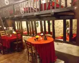 Ambiance d'une auberge moyen âge avec tables dressées de nappes rouges, poutres apparentes et murs en pierre.