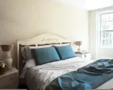 Habitación con cama matrimonial, almohadas azules y manta a juego. Las medidas de camas varían, pero esta parece cómoda.