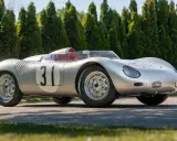 Silberner Porsche 718 RSK mit Startnummer 31, bereit für die Rennstrecke, vor einer Reihe von grünen Bäumen.