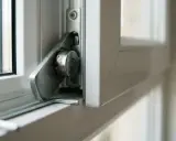 Detalle del mecanismo cierre ventana abatible, con palanca metálica y pivote.