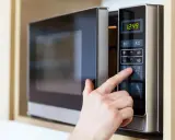 Finger drückt auf die "10" auf dem Bedienfeld einer Mikrowelle, um die Kochzeit einzustellen. Die Mikrowelle zeigt die aktuelle Uhrzeit an.