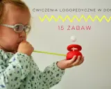 Dziecko w okularach dmucha przez słomkę na drewnianą zabawkę z kulką.