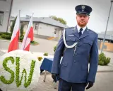 Mężczyzna w mundurze galowym SW, biało-zielony wieniec z napisem SW, polskie flagi.