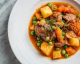 Un savoureux navarin d'agneau recette, garni de pois, carottes et pommes de terre, dans une assiette blanche sur fond marbre.