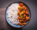 Schüssel mit weißem Reis und würzigem Bang Bang Chicken, garniert mit Koriander und Sesam.