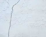 Un muro de casa blanco con una grieta oscura que lo atraviesa. La textura es rugosa y desigual.