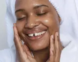 Visage radieux d'une femme souriante, peau hydratée après l'utilisation de rétinol. Elle porte une serviette sur la tête et un peignoir blanc.
