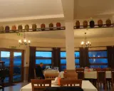 Wnętrze restauracji z oknami wychodzącymi na góry, stoły nakryte obrusami, a na półce nad nimi słoiki z przetworami.