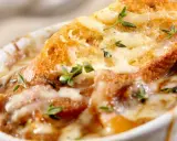 Una ricca zuppa di cipolle toscana, con crostini dorati e formaggio fuso, guarnita con timo fresco.