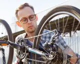 Mężczyzna w okularach sprawdza rozmiary kół rowerowych, skupiony na mechanizmie przerzutek i łańcuchu.
