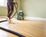 Mann bearbeitet einen Holzboden mit einer Schleifmaschine. Der Parkettboden schleifen ist eine wichtige Arbeit für die Renovierung.