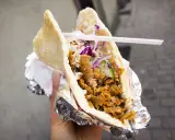 Pyszny kebab w bułce z mięsem, warzywami i sosem. To danie, które swoją popularność zawdzięcza podróżom i wymianie kulturowej, pokazując skąd pochodzi kebab.