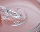 Goccia di siero trasparente con bollicine, su sfondo rosa. Un tocco di vitamina B3 per il viso.