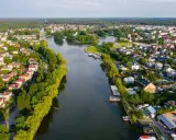 Malowniczy widok na Augustów i jego atrakcje: rzeka, zielone brzegi, domy i las w tle.