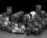 Collezione di obiettivi fotografici di varie dimensioni, dai teleobiettivi ai grandangolari, disposti su sfondo nero. Un vero tesoro per ogni appassionato di termini fotografici.