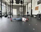 Frau macht Liegestütze im Fitnessstudio, ein Teil ihres plyometrischen Trainings. Hanteln und Medizinbälle liegen bereit.