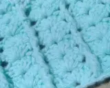 Textura de un tejido a crochet en tono azul claro. Se aprecian los detalles de un punto fantasía, creando un patrón con relieve y pequeños huecos.