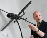 Mann erklärt ein Modell von lba drohnen, das auf einem Stativ steht.
