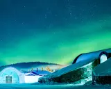 Snöklädda byggnader under norrsken. En magisk plats att se norrsken i Sverige.