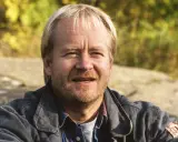 En leende svensk manlig skådespelare från 2000-talet, med blont hår och skäggstubb, bär en jeansjacka.