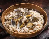 Un delicioso arroz con almejas, servido en un cuenco de madera. Las almejas, abiertas y jugosas, se mezclan con el arroz cremoso.