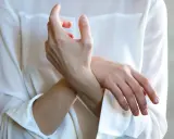 Frau hält sich das Handgelenk, als ob sie einen stechenden Schmerz im Handgelenk bei Drehbewegung spürt.